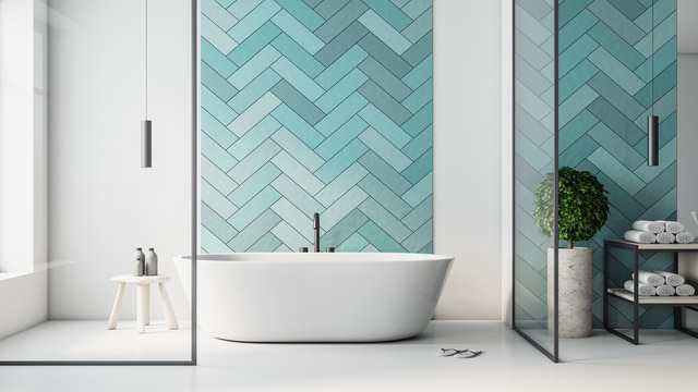 Salle de bain moderne avec baignoire îlot, mur carrelé turquoise à chevrons, et douche en verre. Planté et étagère de serviettes.